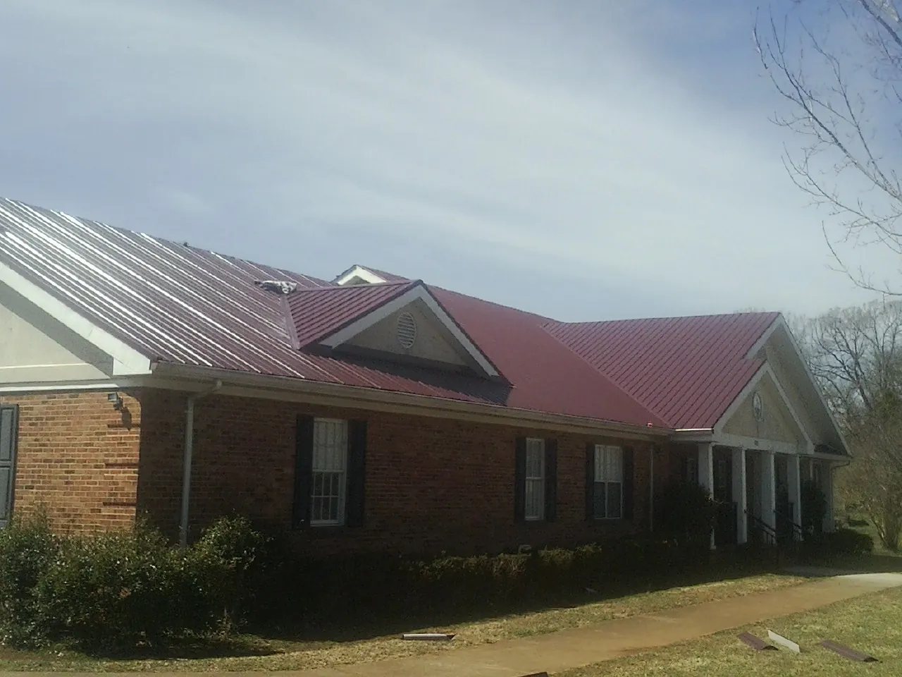 Red metal roof with gabled entries on a long brick building, from a Hail Damage Roof Repair job in Peaks Island