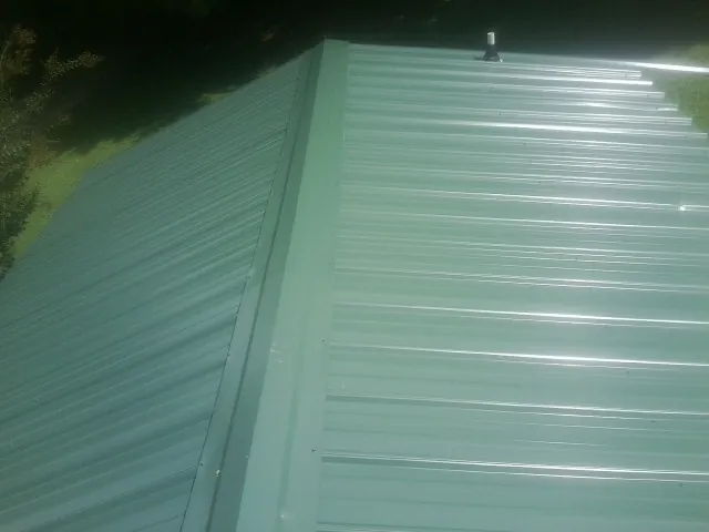 New green metal panels meeting at the ridge of a roof — Flat Roof Repair work by our crew in Peaks Island