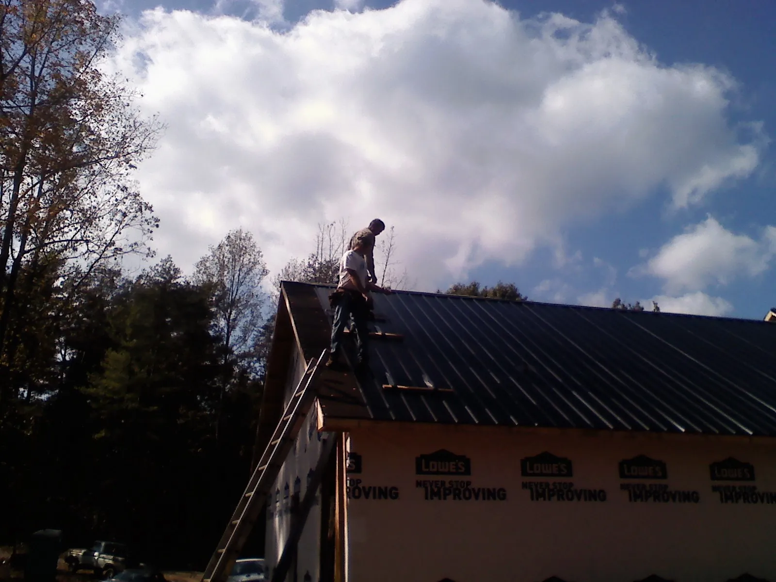 Roofer fastening dark metal panels high against a cloudy sky, from a Roof Inspection job in Peaks Island