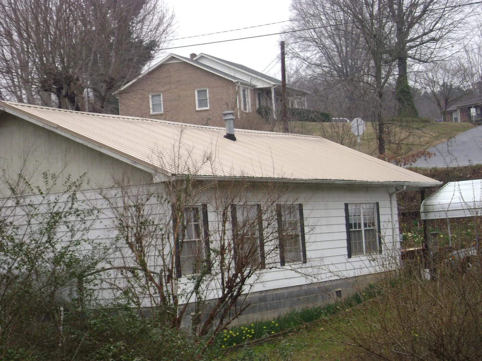 Tan metal roof on a white sided house set into a hillside — Commercial Roofing by Roofing Brothers in Peaks Island