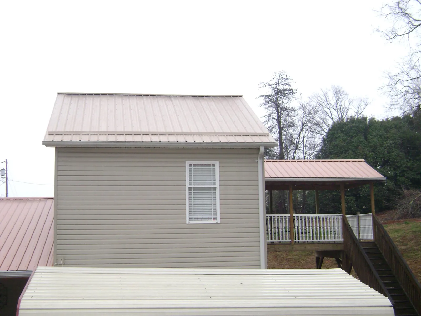 Tan metal roofs on a two story addition and attached porch, from a Roof Replacement job in Peaks Island